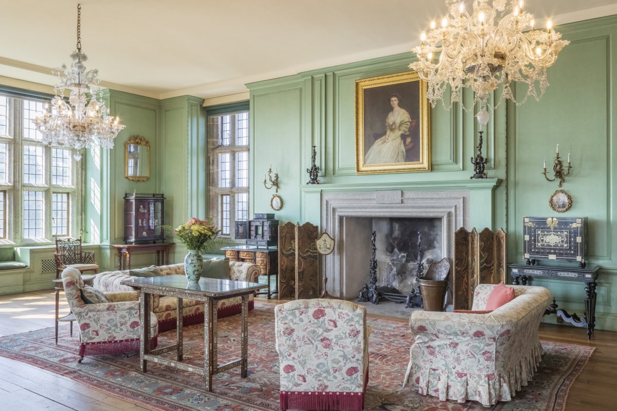 Light green walls adorned with paintings. Two large chandeliers hanging from the ceiling.