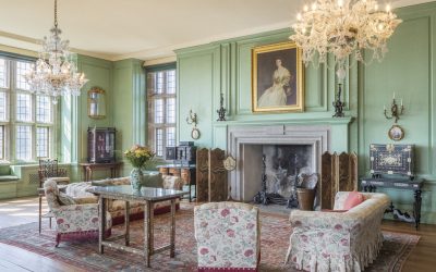 Light green walls adorned with paintings. Two large chandeliers hanging from the ceiling.