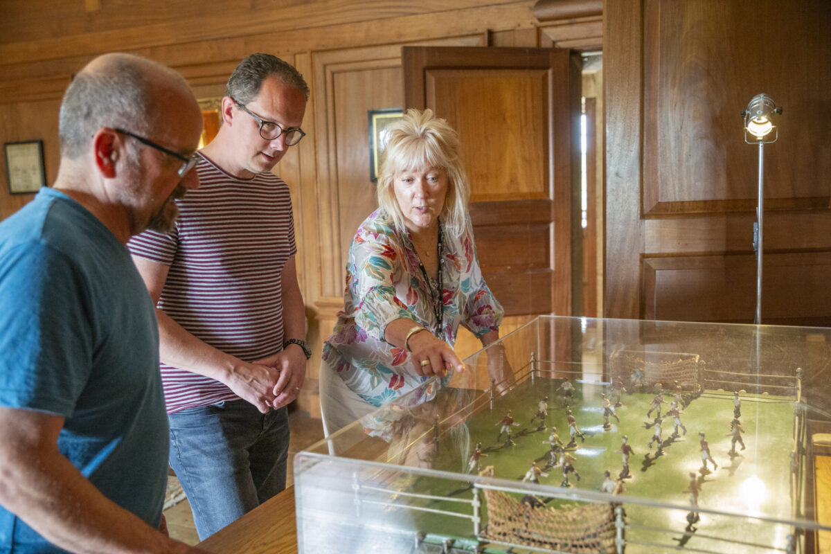 A female volunteer is showing two visitors the Subbuteo table in the Nursery at Castle Drogo.